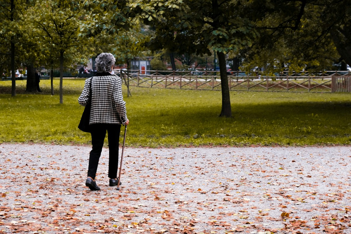 Persona adulta caminando con un bastón por un parque